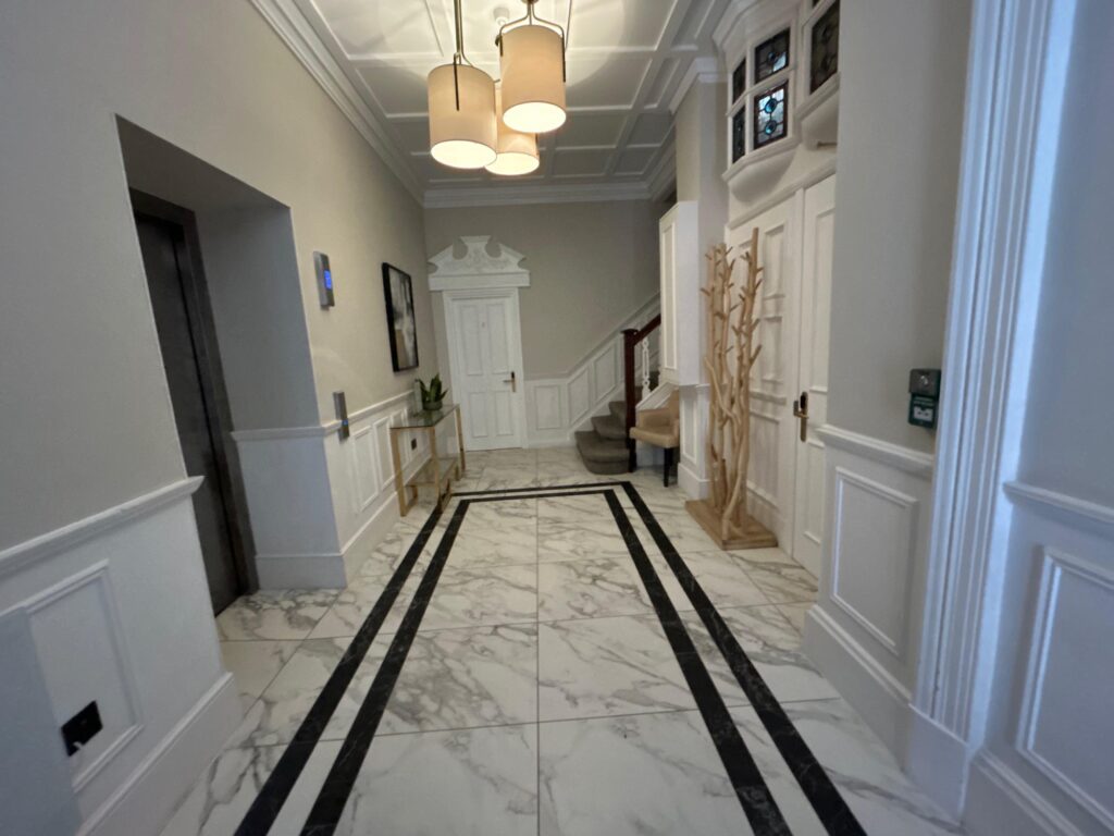 Entrance hall with white marble floor inlaid with black banding, pendant lights and panelled walls