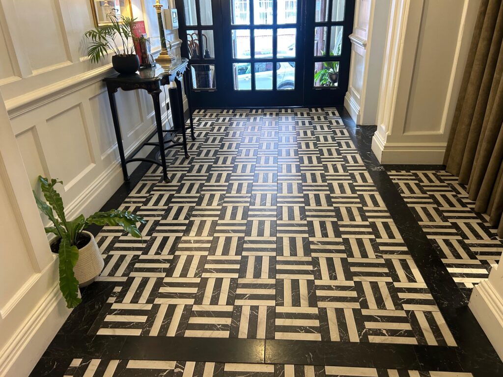 Hallway with black-and-white basket-weave marble floor, panelled walls and glazed front doors