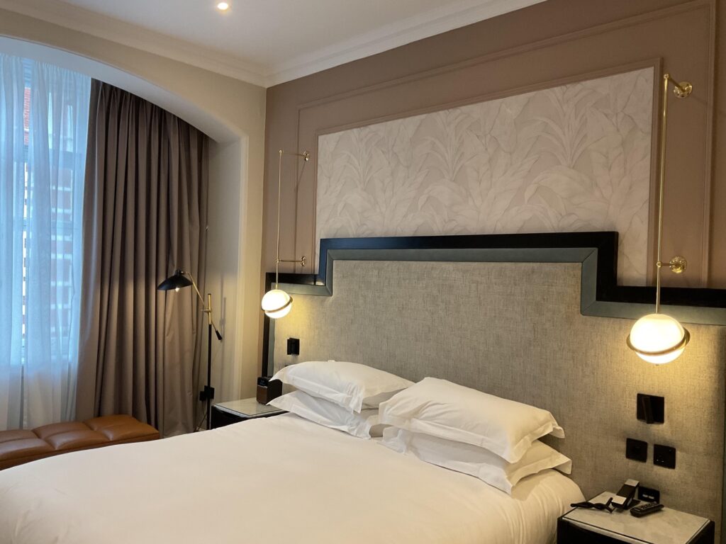Hotel bedroom with upholstered headboard, brass wall lights and white bedding