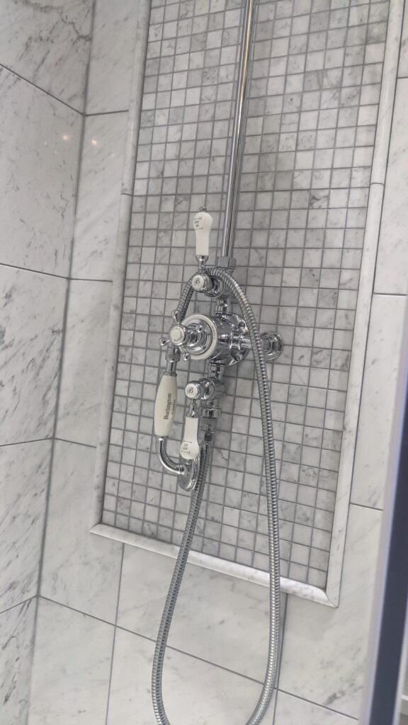 Marble shower with exposed chrome thermostatic valve and mosaic-tiled niche
