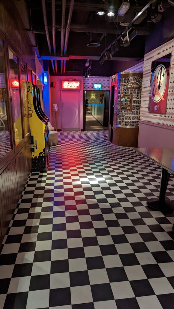 Entrance corridor with black-and-white chequered floor and neon signage
