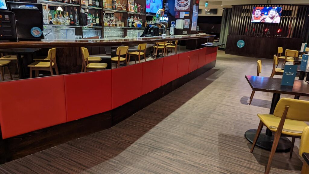 Long bar with red panelled front, yellow bar stools and back-lit shelving