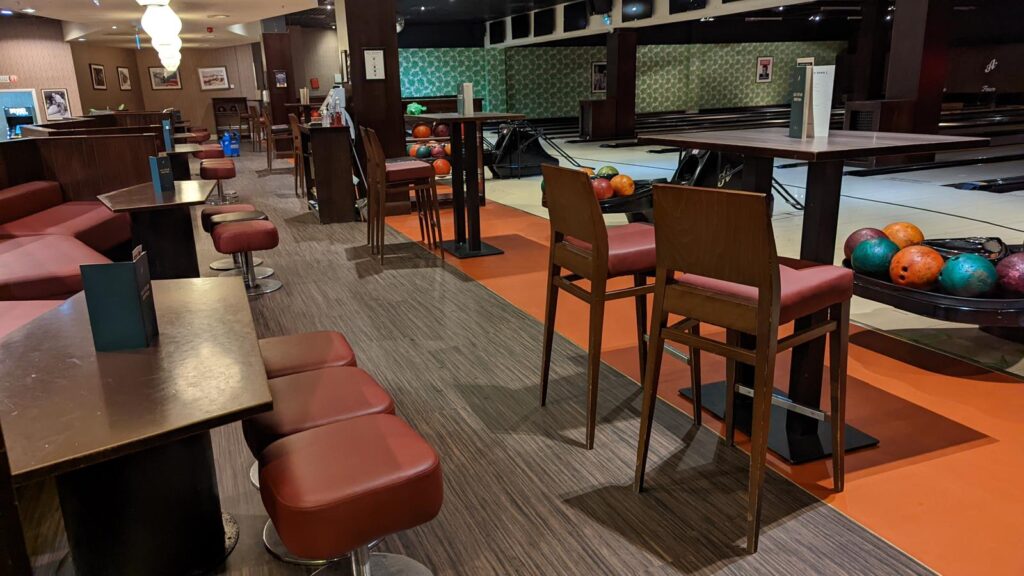 Lane-side seating with red stools, timber tables and bowling balls on a rack