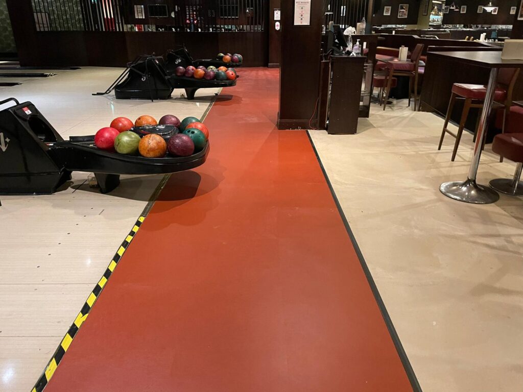 Orange walkway beside the lanes with ball returns and bar seating