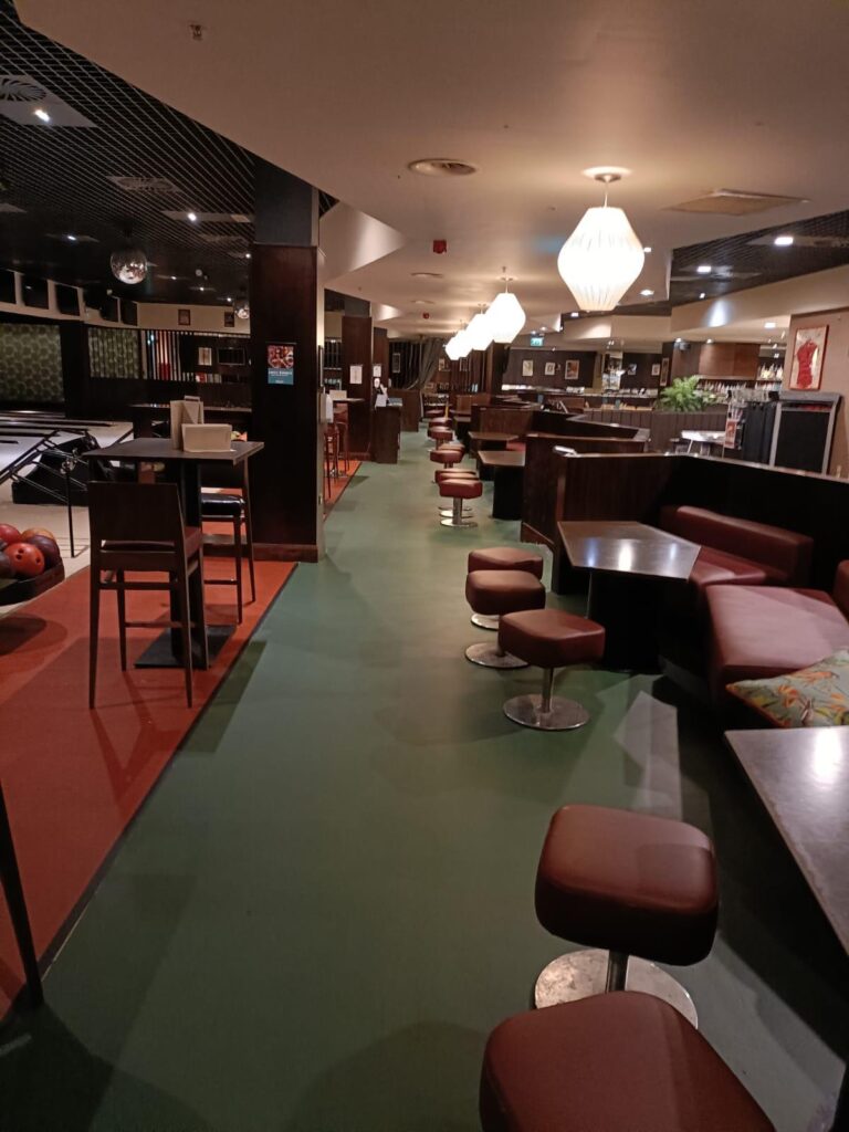 Seating area beside the lanes with red stools on a green and orange floor