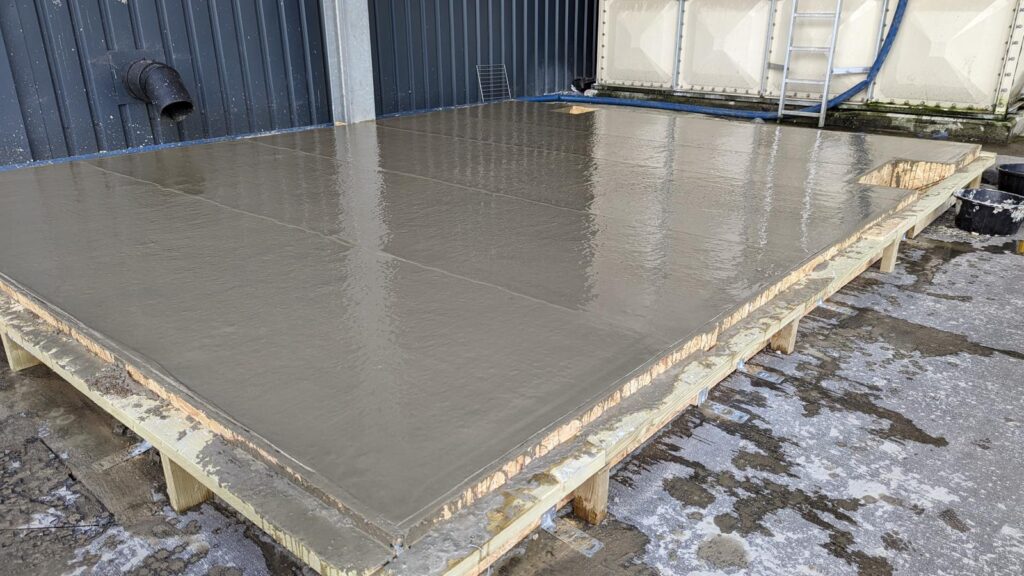 Freshly laid concrete slab inside timber formwork beside a building