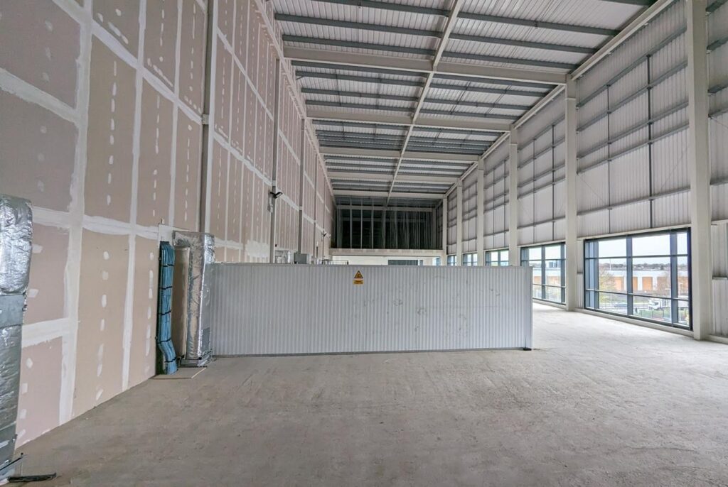 Empty unit mid-build with boarded walls, exposed roof structure and full-height windows